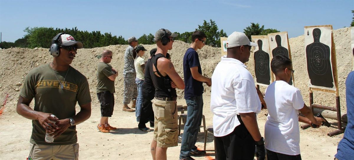 Jason in a ball cap and hearing protection watching over a group at an outdoor firing range.