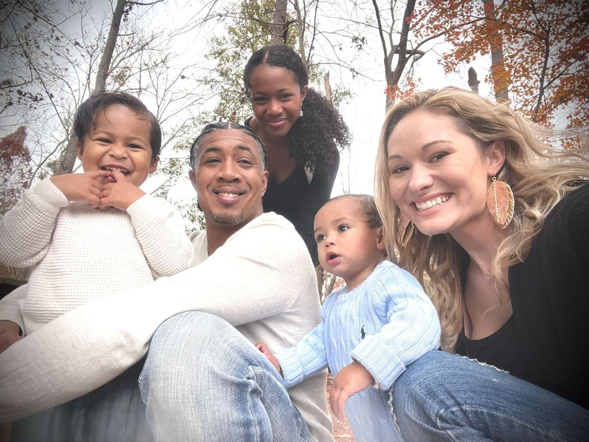 Jason, Ellie, and their three children smiling together among autumn trees.