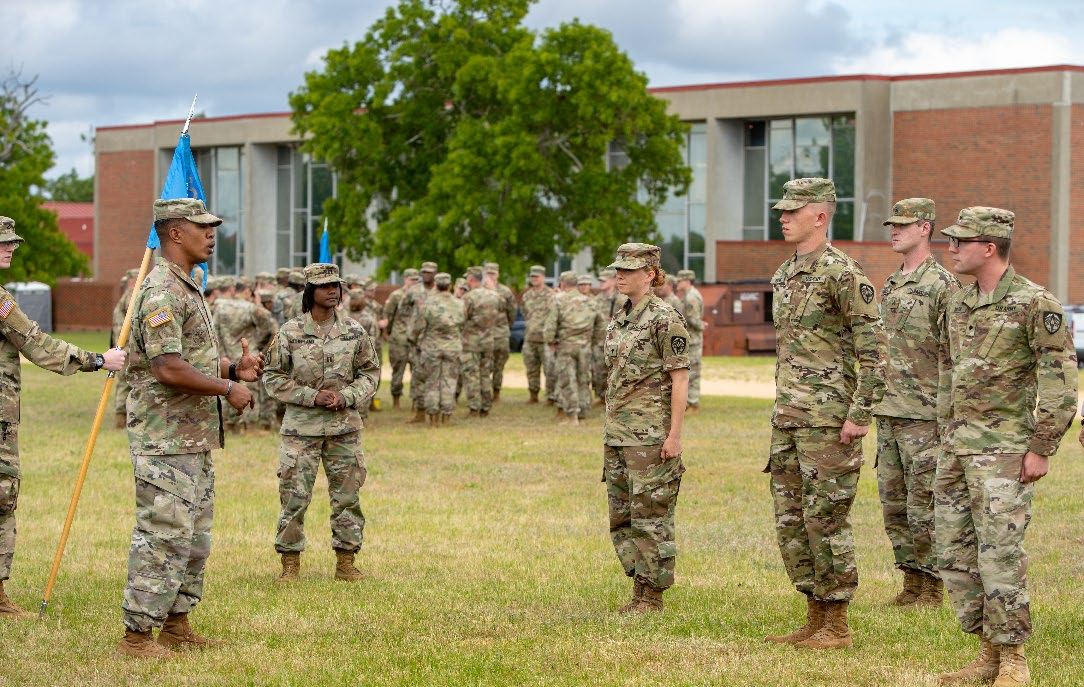 Jason holding a unit guidon on a parade field with soldiers standing in formation.