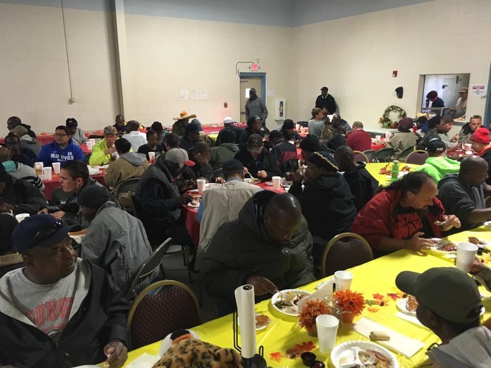 A dining hall full of guests being served Thanksgiving meals.